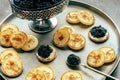 Blinis with black caviar and cream cheese, on a festive dish on black