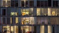 Windows of the multi-storey building of glass and steel lighting inside and moving people within Royalty Free Stock Photo