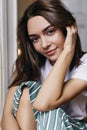 Blissful girl with dark eyes playing with her brown hair. Indoor portrait of pleasant female model