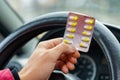 Blister of pills in the hands of the driver on a blurred background of the steering wheel in the car