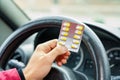 Blister of pills in the hands of the driver on a blurred background of the steering wheel in the car