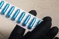 Blisters with blue tablets in hand in a rubber glove. On a light background. Close-up. Royalty Free Stock Photo