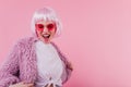 Blithesome girl in periwig dancing on pink background. Excited young woman in peruke expressing hap