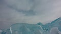 A block of shiny turquoise ice hummocks against the sky.