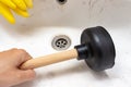 Blocked sewer, clogged wash bowl, basin drain, yellow rubber gloves and a hand holding a plunger in the bathroom at home, plumbing Royalty Free Stock Photo