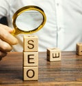 Blocks with the word SEO and a magnifying glass in the hand of a businessman. Search Engine Optimization. Increase the quality and Royalty Free Stock Photo