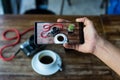 Blogger hand holding smart phone taking photo of coffee and camera on table. Royalty Free Stock Photo