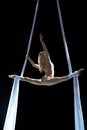 Blond aerial performer with white aerial silks isolated on black background