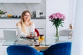 Blond attractive woman kitchen drinking herb citron tea teapot, laptop. Flowers Royalty Free Stock Photo