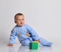 Blond baby boy toddler in blue cotton jumpsuit with rainbow and tiger sits on the floor leaning on his arm