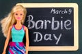 Blond Barbie doll and blackboard with words Barbie Day March 9th