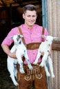 Blond bavarian man holding two little white goats Royalty Free Stock Photo