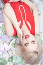 A beautiful blonde woman in a red dress is lying on a lot of money and enjoying life. rich caucasian girl top view