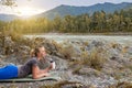 Blond beautiful girl lying on the mat on the stone ground drinking coffee or tea, resting after sport outdoors in the mountains Royalty Free Stock Photo