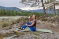 Blond beautiful girl sitting on the mat on the stone ground drinking coffee or tea, resting after sport outdoors in the mountains Royalty Free Stock Photo