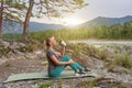 Blond beautiful girl sitting on the mat on the stone ground drinking coffee or tea, resting after sport outdoors in the mountains Royalty Free Stock Photo