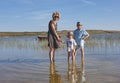 Blond beautiful mother with her two kids, standing in a lake with aquatic plants and a boat, in the background a green landscape Royalty Free Stock Photo