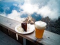 Blond beer and a slice of Sachertorte, mountains, rocks and clouds on the background Royalty Free Stock Photo