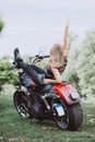 Blond biker girl sitting on a motorcycle and raised her hand up rear view. Soft focus Royalty Free Stock Photo