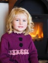 Blond blue eyed little girl sitting in front of a fireplace
