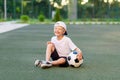 A blond boy in a cap in a sports uniform sits on a football field with a soccer ball, sports section. Training of children, Royalty Free Stock Photo