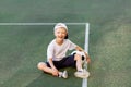 A blond boy in a cap in a sports uniform sits on a football field with a soccer ball, sports section. Training of children, Royalty Free Stock Photo