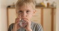 Blond boy drinks water from a glass and shows the class. Joyful child with pleasure drinks water.