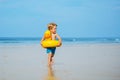 Blond boy with inflatable yellow duck buoy run on the sand beach Royalty Free Stock Photo