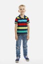 A blond boy in jeans and a multicolored T-shirt stands. White background. Vertical. Full height