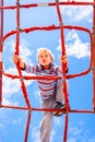 Blond boy perched on a web rope-ladder structure in a children`s playground for fun climbing Royalty Free Stock Photo