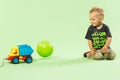Blond boy playing with colorful car toy green background Royalty Free Stock Photo