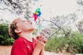 Blond boy playing in a forest with a colorful pinwheel blowing air with funny face Royalty Free Stock Photo