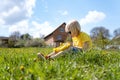 Blond boy sits on the grass and weaves wreath from dandelions. Child rests countryside during summer holidays Royalty Free Stock Photo