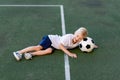 A blond boy in a sports uniform is lying on the football field with a soccer ball, sports section. Training of children, children Royalty Free Stock Photo