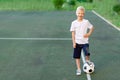 A blond boy in a sports uniform stands on a football field with a soccer ball, sports section. Training of children, children`s Royalty Free Stock Photo