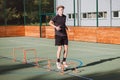 Blond boy in sportswear jumps over red hurdles to improve lower body dynamics. Plyometric training in an outdoor environment.