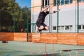 Blond boy in sportswear jumps over red obstacles to improve lower body dynamics. Plyometric training in an outdoor environment.