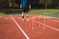 Blond boy in sportswear jumps over red obstacles to improve lower body dynamics. Plyometric training in an outdoor environment.