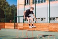 Blond boy in sportswear jumps over red obstacles to improve lower body dynamics. Plyometric training in an outdoor environment.