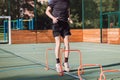 Blond boy in sportswear jumps over red obstacles to improve lower body dynamics. Plyometric training in an outdoor environment.