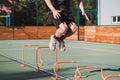 Blond boy in sportswear jumps over red obstacles to improve lower body dynamics. Plyometric training in an outdoor environment.