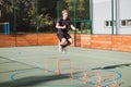 Blond boy in sportswear jumps over red obstacles to improve lower body dynamics. Plyometric training in an outdoor environment.