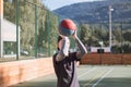 Blond boy in sportswear practices shooting a basketball from behind the three-point line. Outdoor basketball court. Preparing for