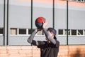 Blond boy in sportswear practices shooting a basketball from behind the three-point line. Outdoor basketball court. Preparing for