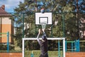 Blond boy in sportswear practices shooting a basketball from behind the three-point line. Outdoor basketball court. Preparing for