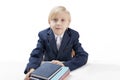 Blond boy of 7-8 years old in jacket or school uniform sits at table with stack of notebooks and notebooks. Portrait of schoolboy