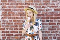 Blond Caucasian Girl Licks Ice Cream Against a Brick Wall Cone Fedora Hat