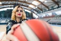 Blond cheerleader in a black jacket holding a ball in front of a camera. Blurred foreground. Sport concept. Royalty Free Stock Photo