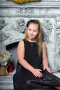 Blond child girl in a black dress by the fireplace Royalty Free Stock Photo