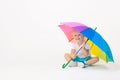 Blond child kid caucasian sits under rainbow bright umbrella and waves his hand on white background isolated